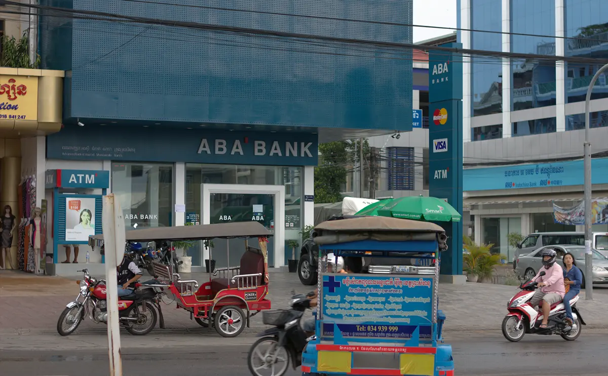 An ABA Bank branch in Sihanoukville with street-side ATM booths and Visa and Mastercard signs, tuk-tuks passing in front