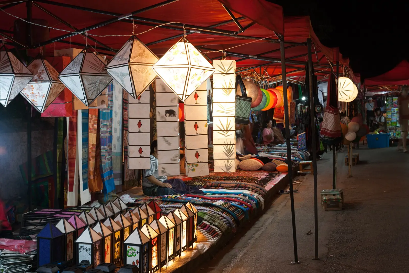 The Luang Prabang night market at dusk, paper lanterns lit above stalls of textiles and handicrafts