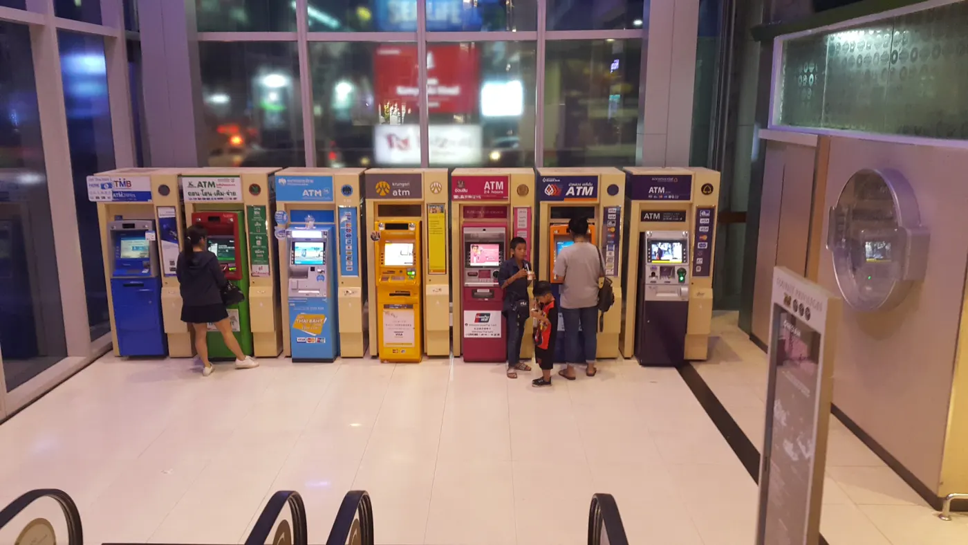 A row of ATMs from eight different Thai banks lined up side by side in a Bangkok shopping mall